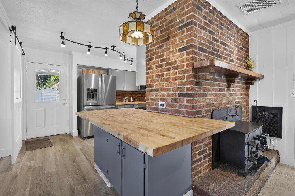 Kitchen with a butcher-block island beside a large brick fireplace and wood-burning stove.