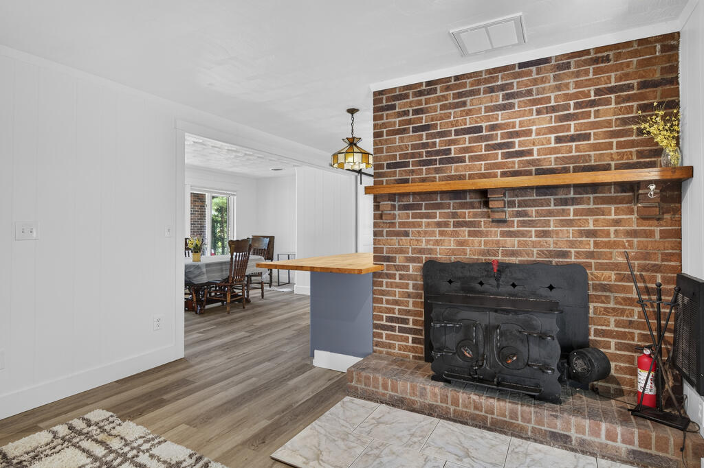 Living room with a brick fireplace, black wood-burning stove, and wooden mantel beside an open dining area.