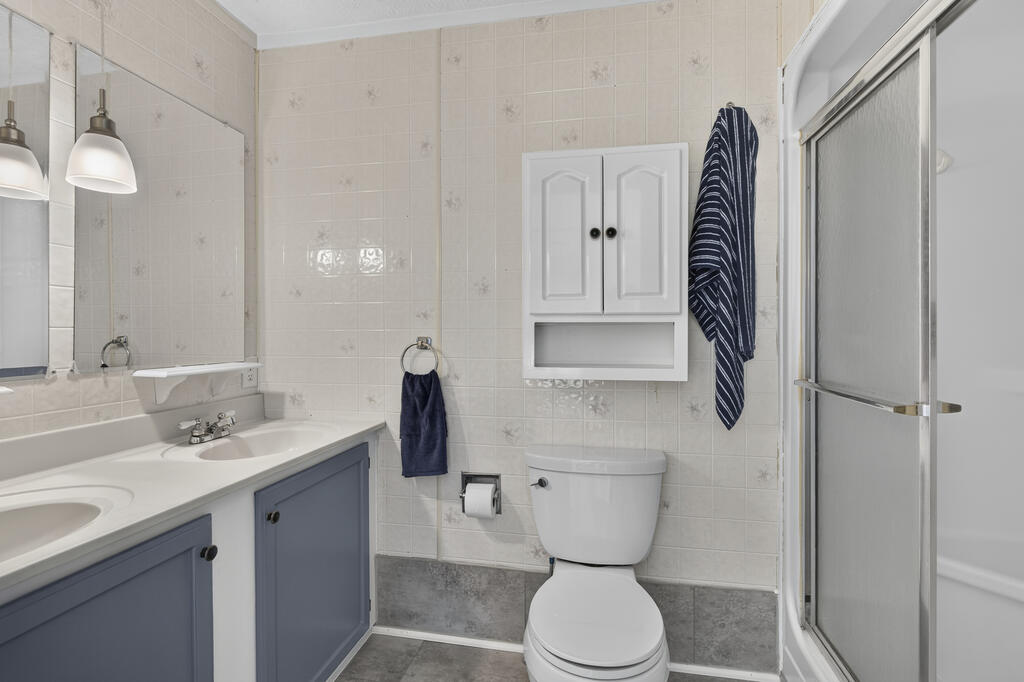 Bathroom with blue-gray double vanity, wall cabinet, toilet, and glass shower.