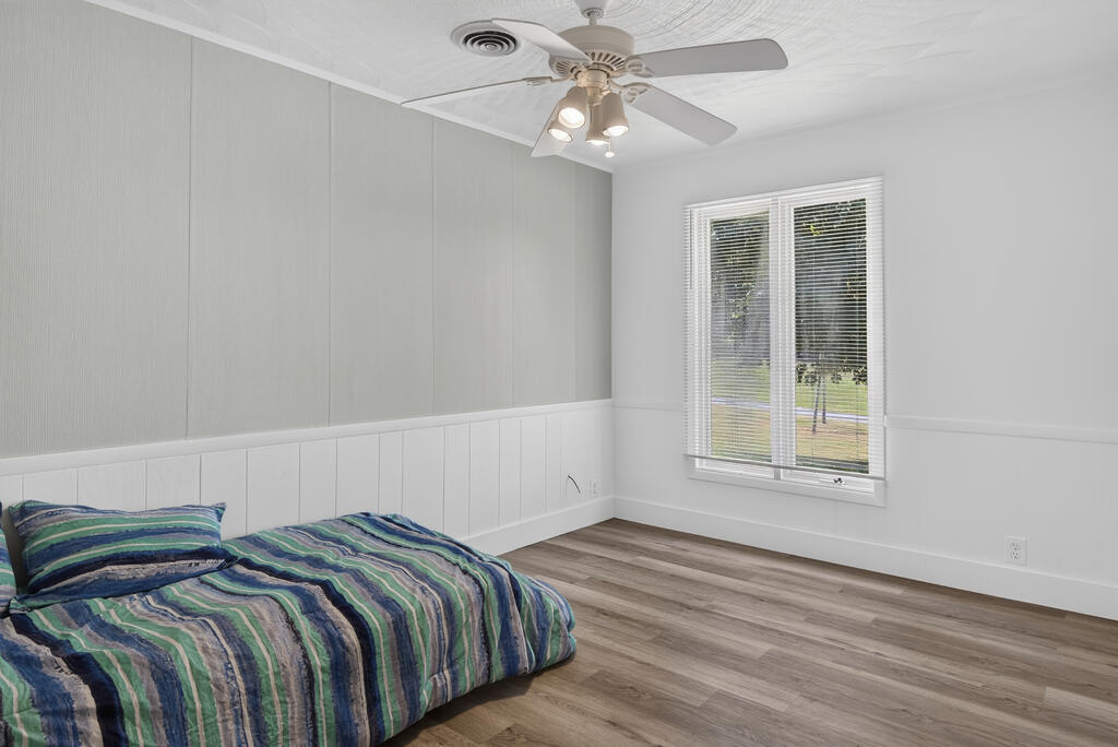 Bedroom with a striped bedspread, paneled walls, ceiling fan, and window overlooking the yard.