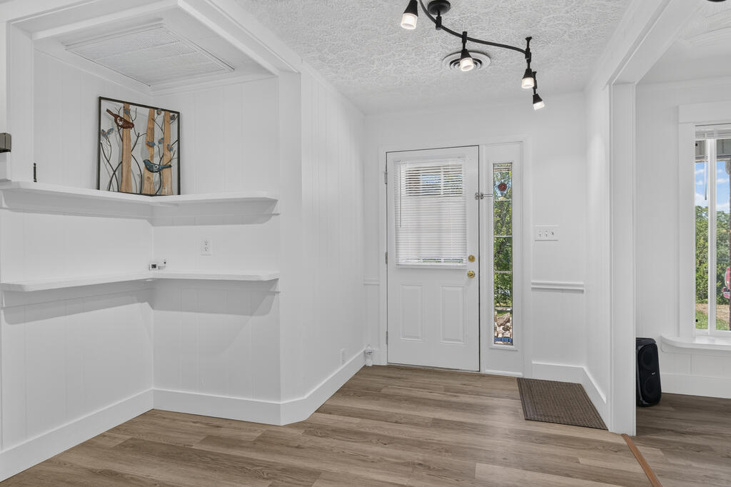 Bright entryway with white built-in shelves, a glass-panel front door, and wood-look flooring.