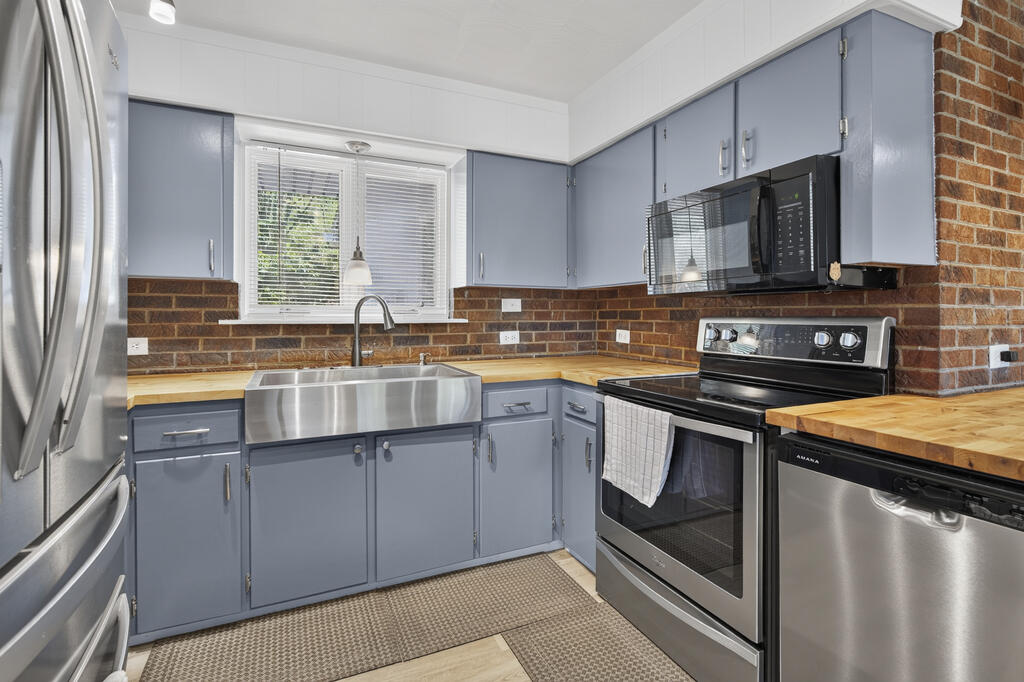 Kitchen with blue-gray cabinets, butcher-block counters, a brick backsplash, and stainless-steel appliances.