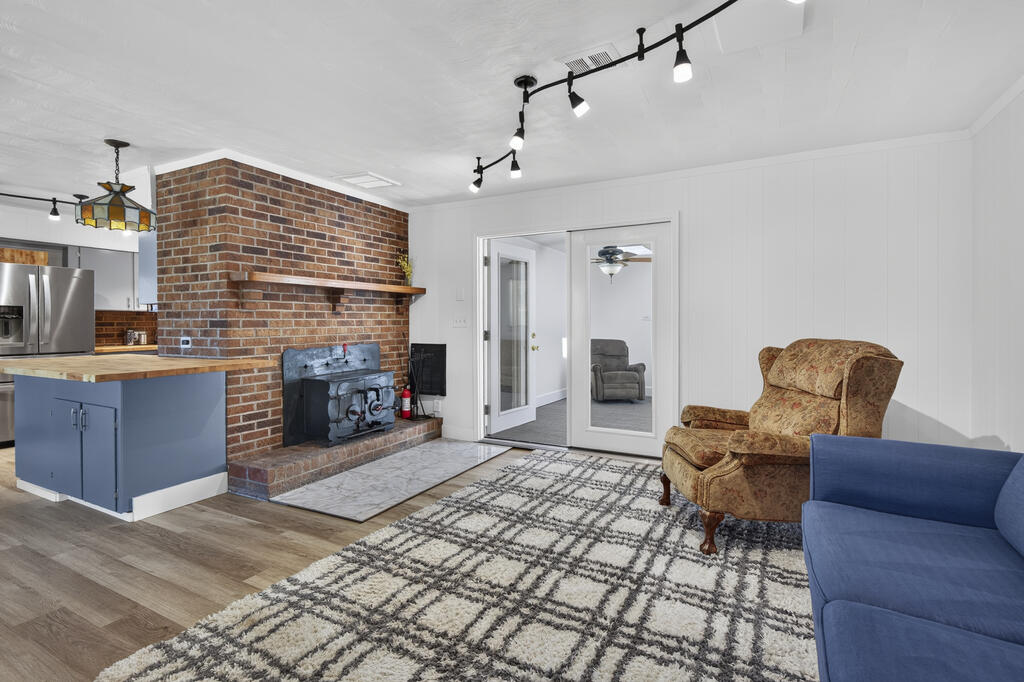 Living room with a brick fireplace and wood stove, blue kitchen island, and patterned rug.