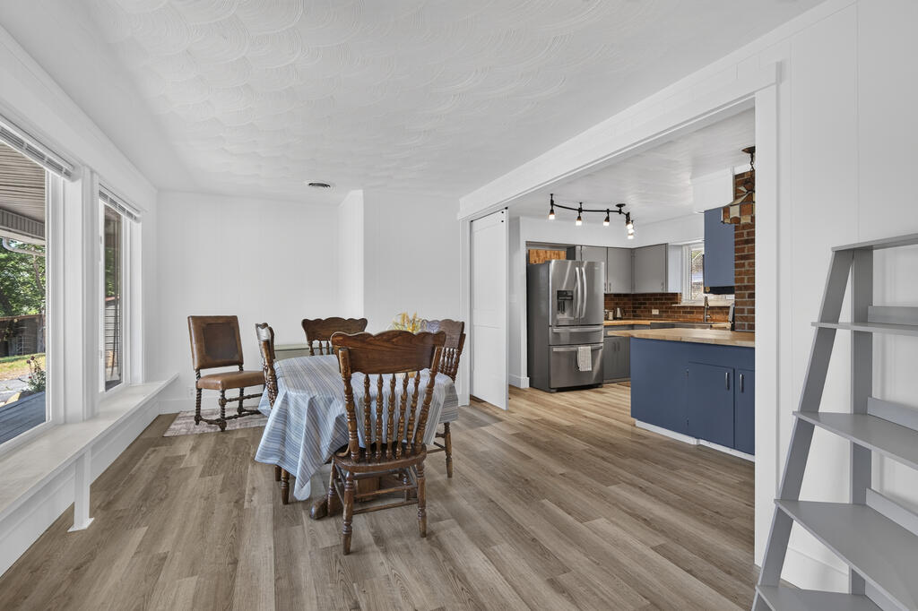 Dining room with a wooden table beside large windows and an open kitchen with blue cabinets.