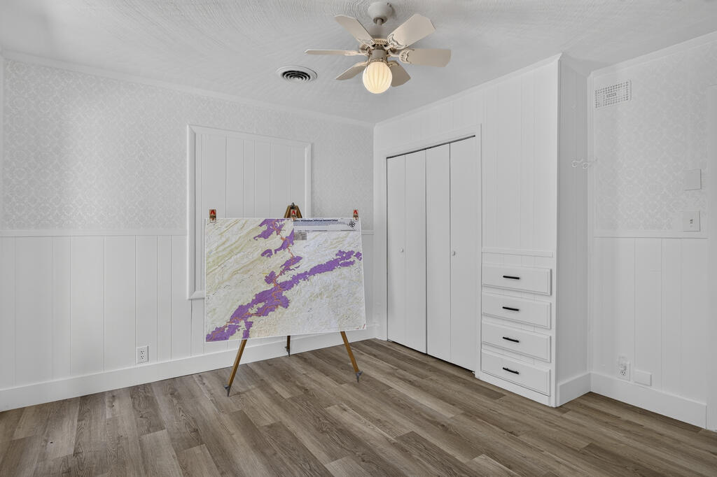 Empty room with a large map on an easel, built-in closet drawers, ceiling fan, and wood-look flooring.