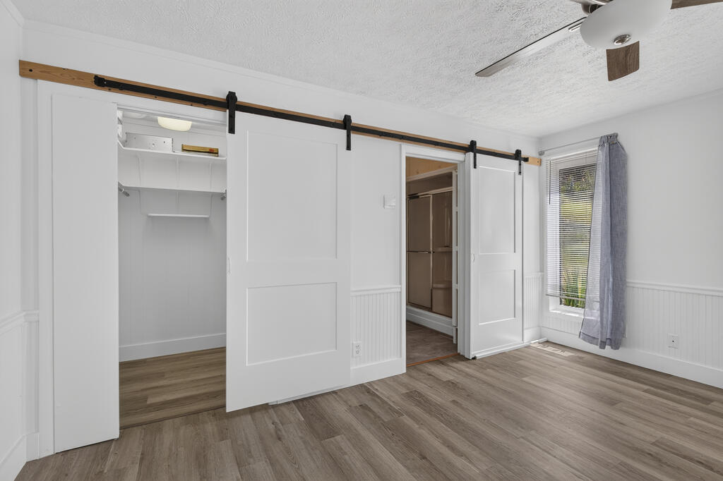Vacant bedroom with sliding barn doors over two closets, wood-look floors, and a curtained window.