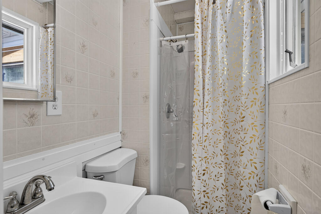Bathroom with beige patterned tile, a white sink and toilet, and a gold-leaf shower curtain.