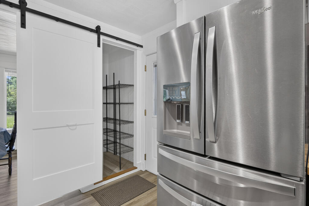 Kitchen with a stainless French-door refrigerator beside an open pantry with wire shelving.