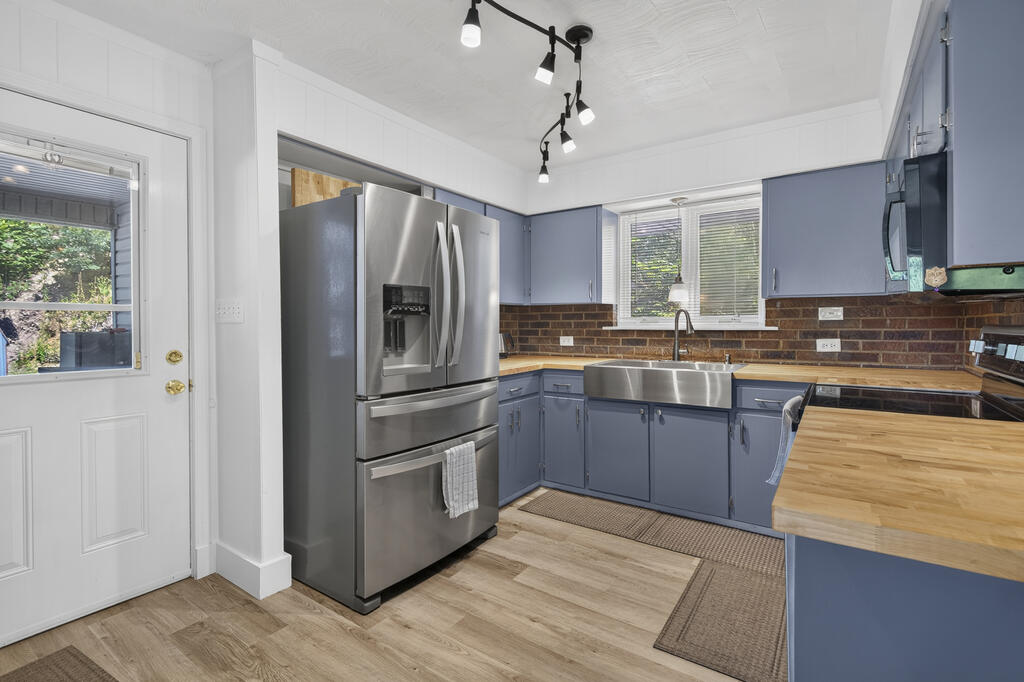 Kitchen with blue cabinets, butcher-block counters, stainless steel appliances, and a large sink.