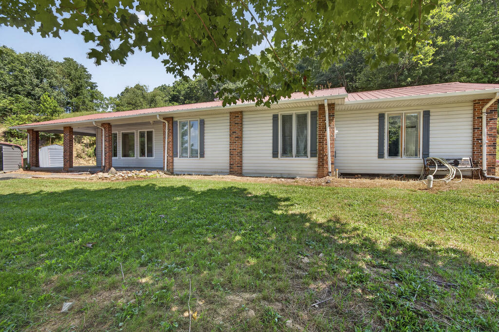 Single-story home with a covered carport, red metal roof, and grassy yard.