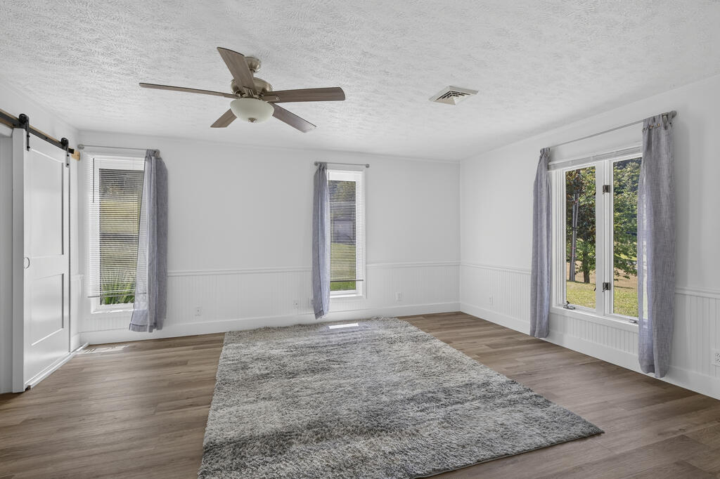 Empty room with a gray rug, wood-look floors, curtained windows, and a ceiling fan.
