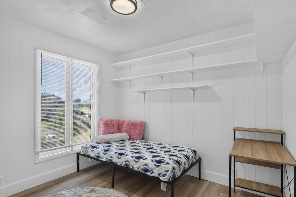Bedroom with a bed beneath wall shelves and a desk beside a large window.