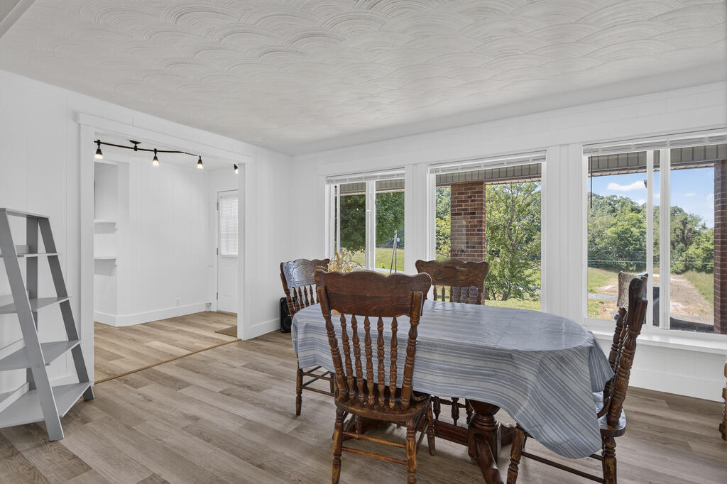 Dining room with carved wooden chairs around a table beside large windows overlooking trees.