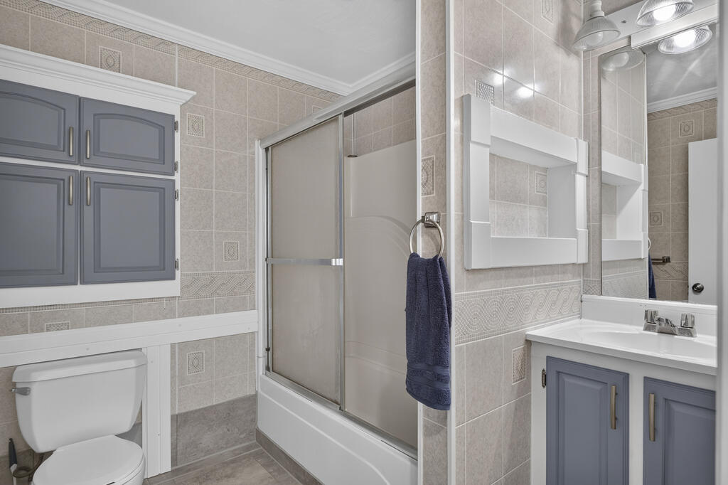 Bathroom with a glass shower, toilet, and gray-cabinet vanity.