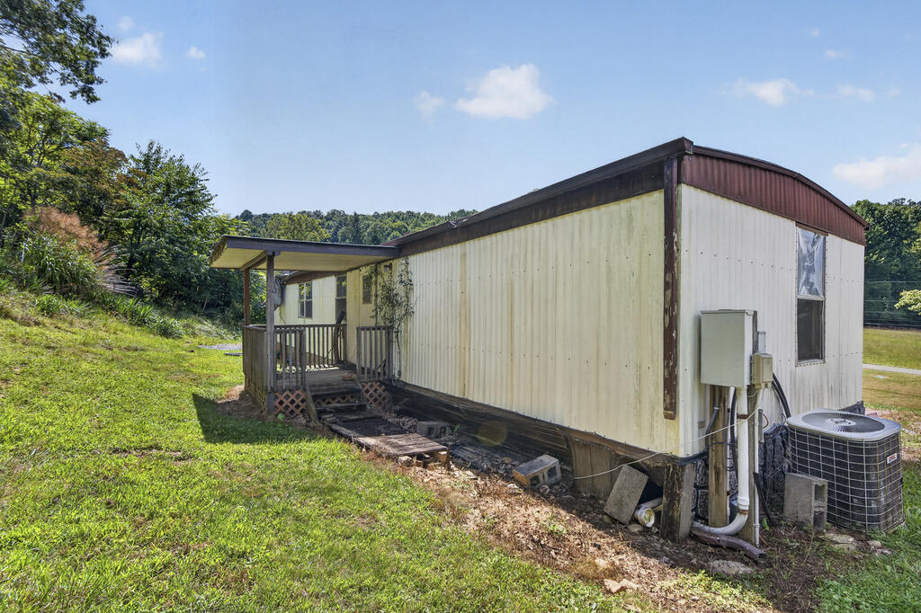 Manufactured home with a covered porch, outdoor air-conditioning unit, and wooded hills behind it.