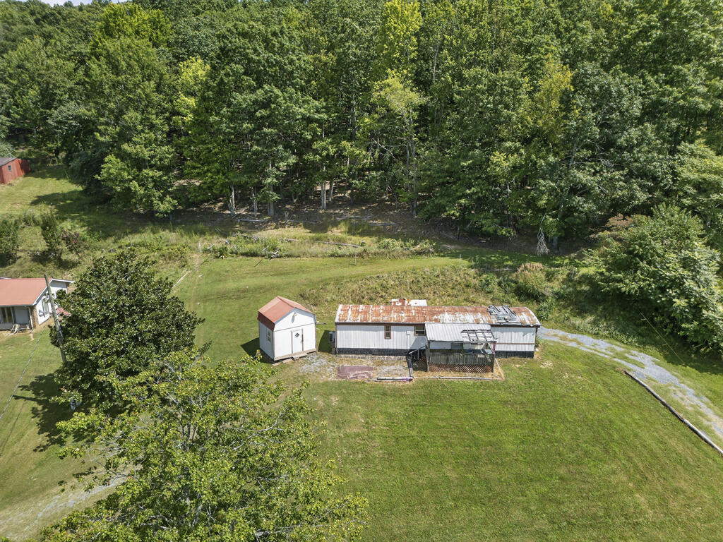 Aerial view of a metal outbuilding and small shed on a grassy property beside woods.
