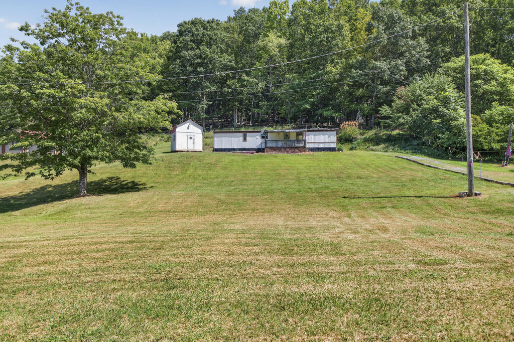 Broad grassy yard with a small shed and low outbuilding beside wooded grounds.