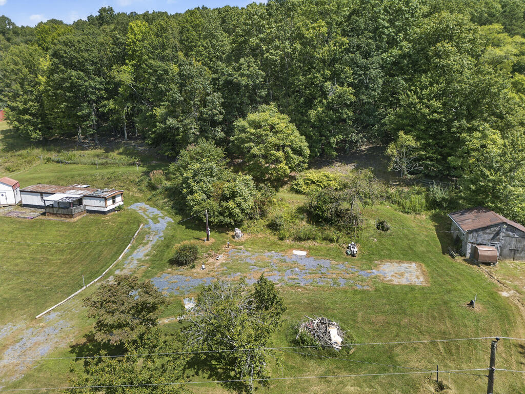 Aerial view of a grassy lot bordered by woods, with small outbuildings and a gravel drive.