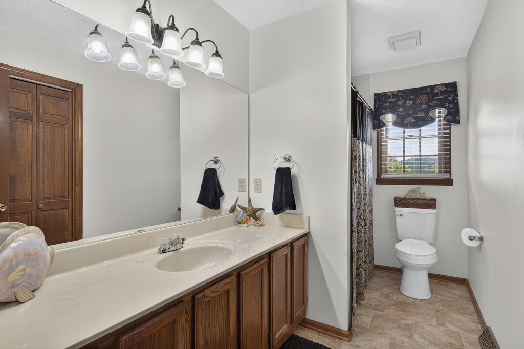 Bathroom with a long wood vanity and mirror beside a separate toilet area with a window.