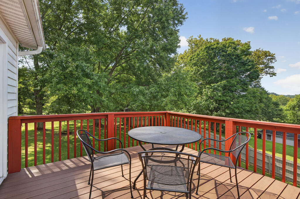 Raised wooden deck with red railings, patio table, and chairs overlooking a tree-filled yard.