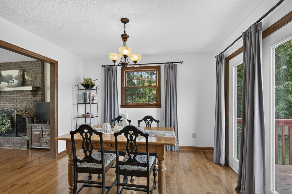 Dining room with a wooden table, black chairs, chandelier, and glass doors opening to a deck.