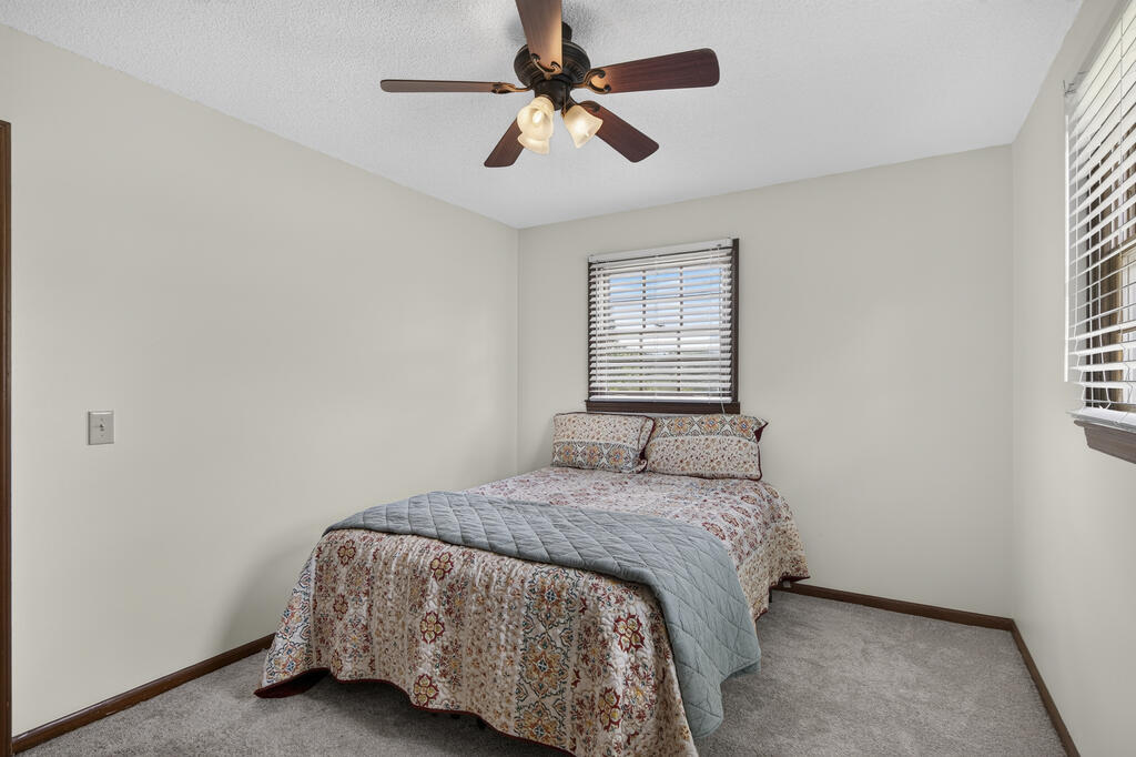 Bedroom with a floral bedspread, gray quilt, ceiling fan, and windows with blinds.