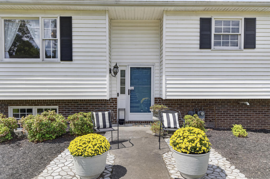 Home entrance with a blue door, striped patio chairs, and pots of yellow flowers.
