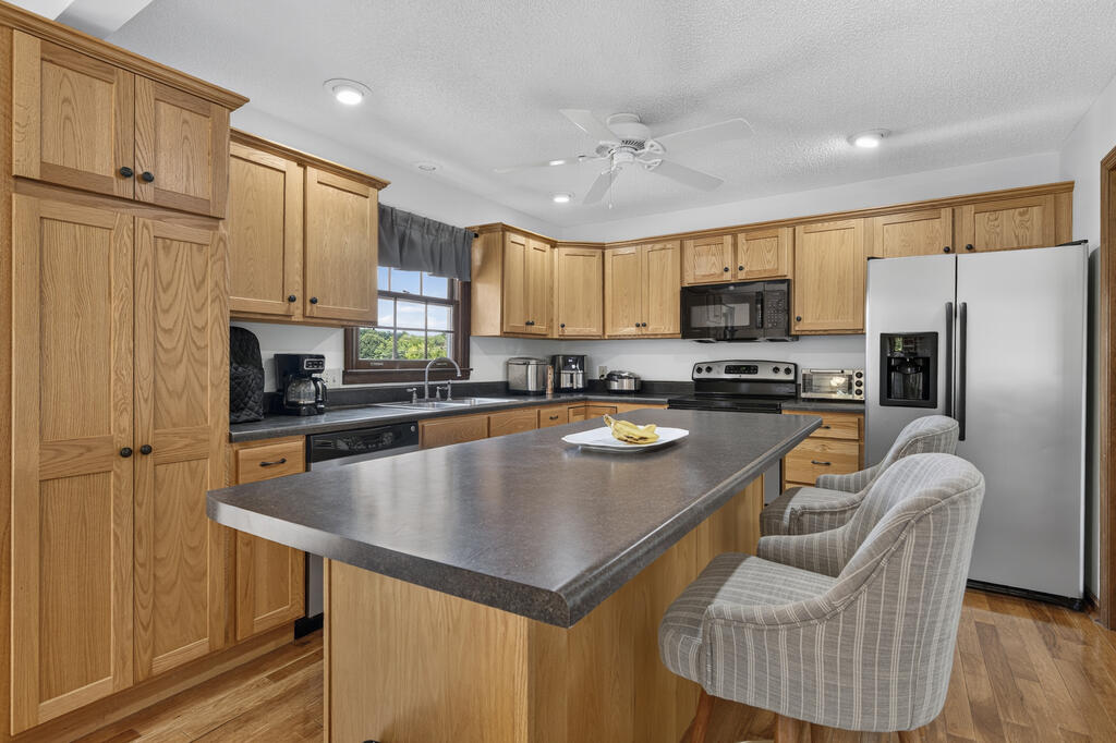 Kitchen with a large island, light wood cabinets, stainless steel appliances, and upholstered bar chairs.