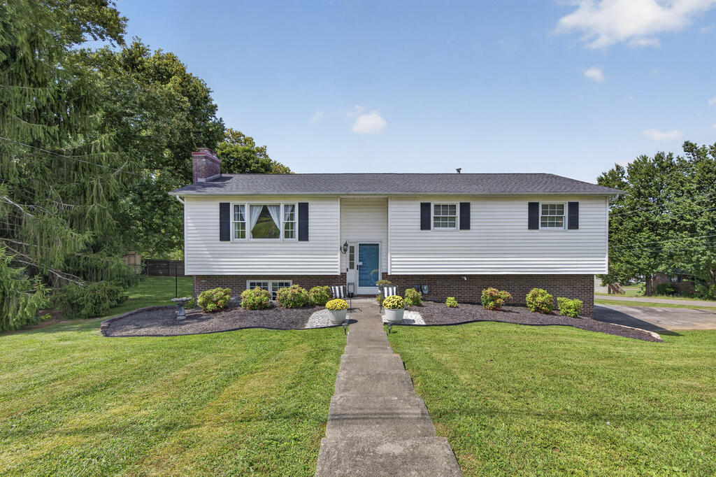 White split-level home with a brick lower facade, blue front door, and walkway through a green lawn.