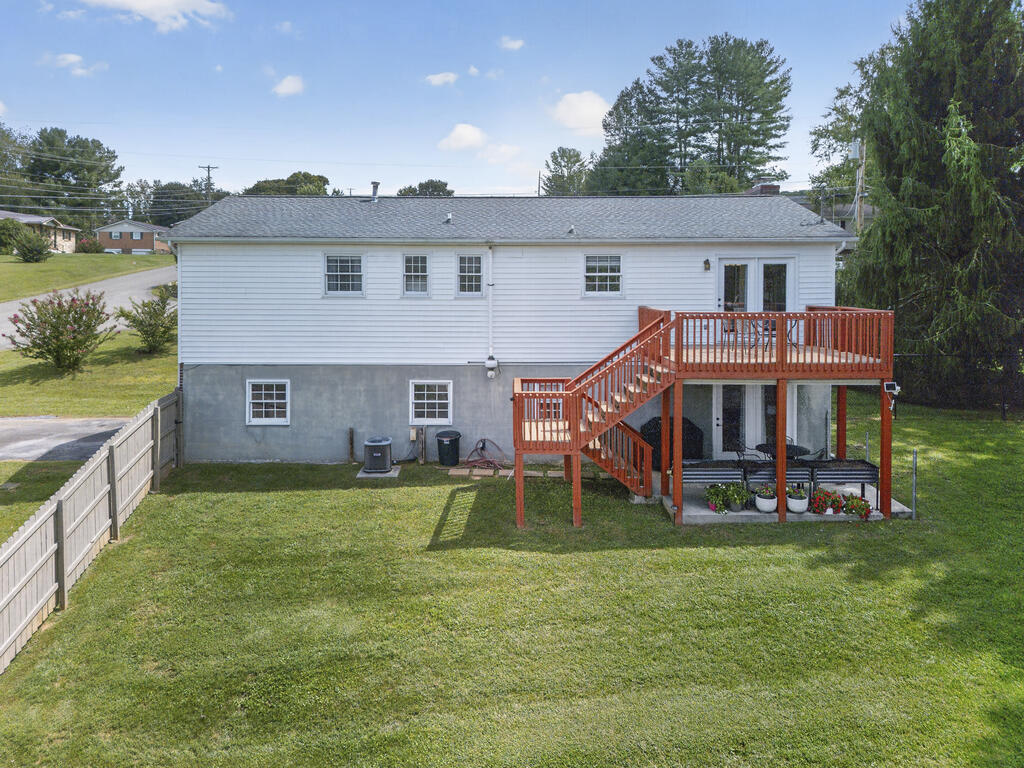 Rear of a white house with a raised wooden deck, stairs, and fenced lawn.