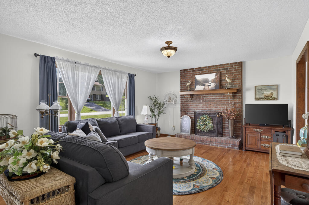 Living room with gray sectional sofas, brick fireplace, and large curtained windows.