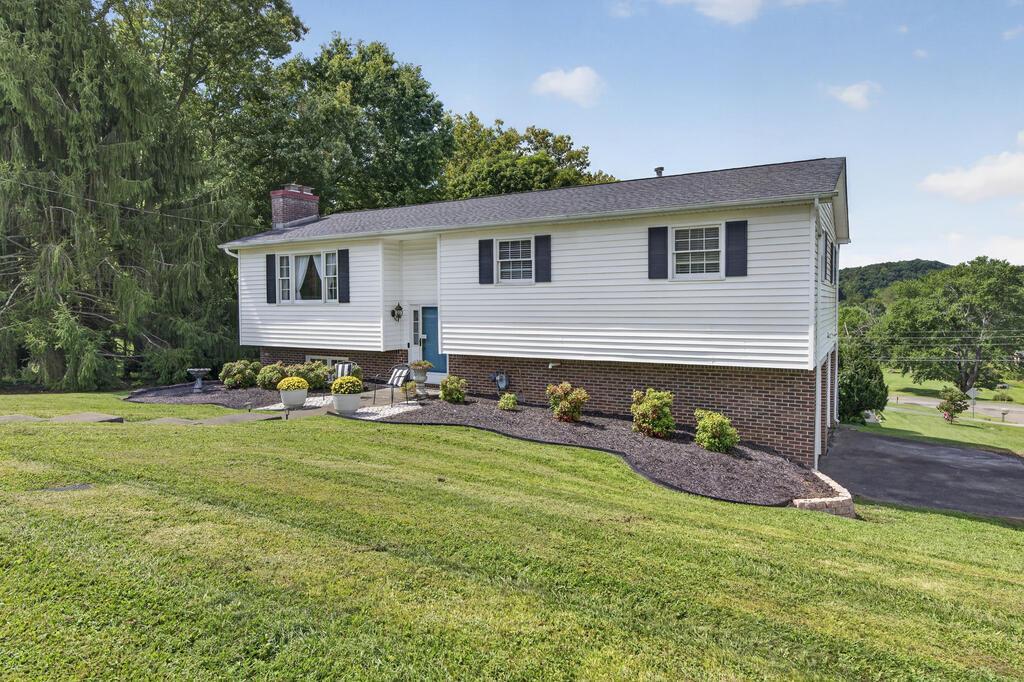 White split-level house with brick lower facade, dark shutters, and a broad sloping lawn.