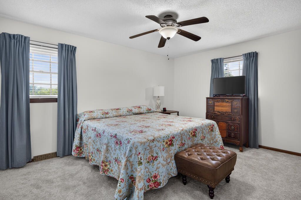 Bedroom with a floral-covered bed, blue curtains, wooden dresser, and tufted leather ottoman.