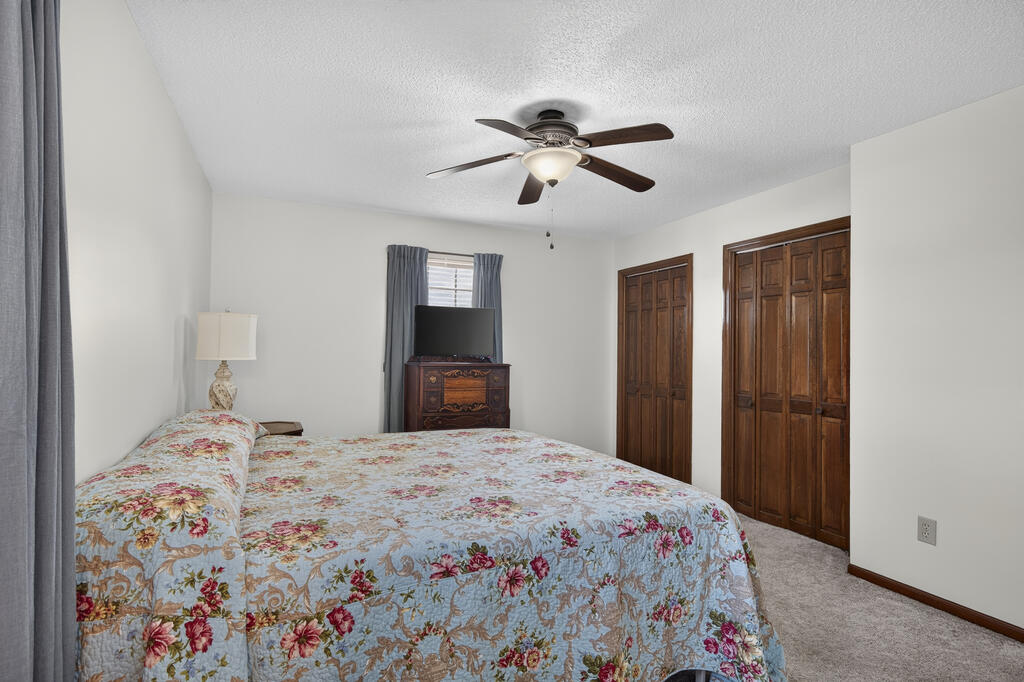Bedroom with a blue floral bedspread, ceiling fan, and two wooden closet doors.
