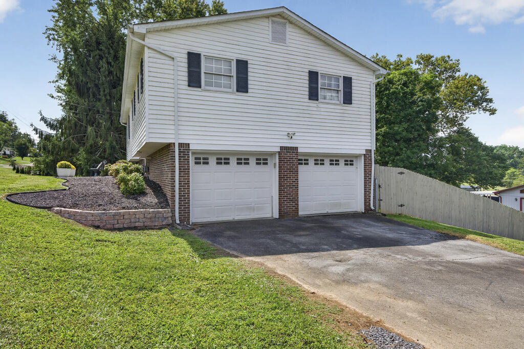 White two-story house with a brick lower level, two garage doors, and a sloped driveway.