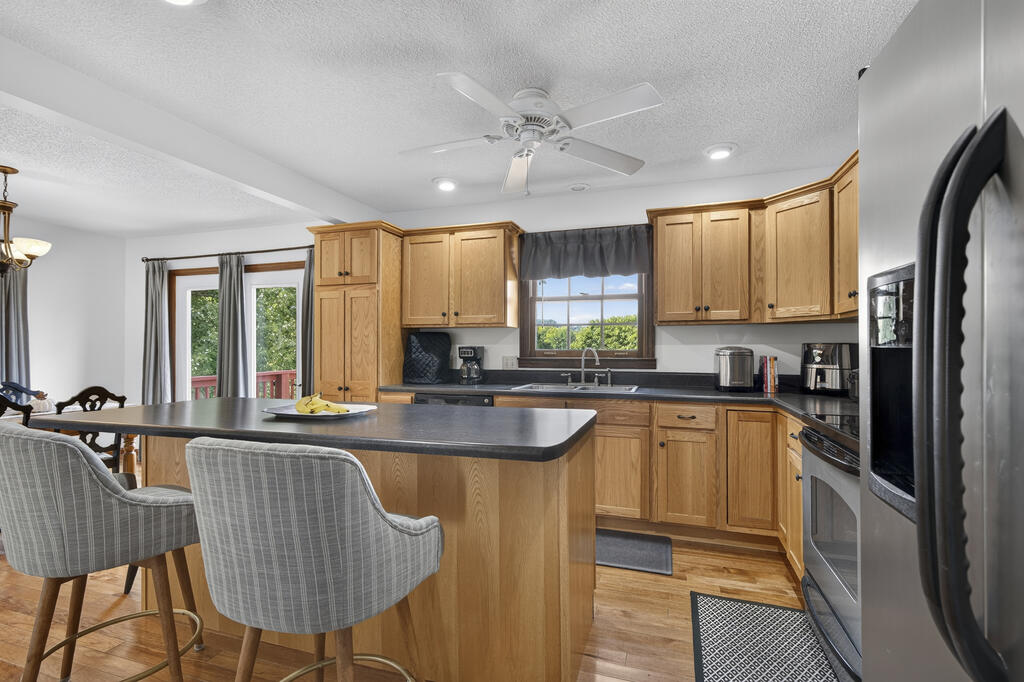 Kitchen with honey-colored cabinets, a large island, stainless steel appliances, and windows overlooking greenery.