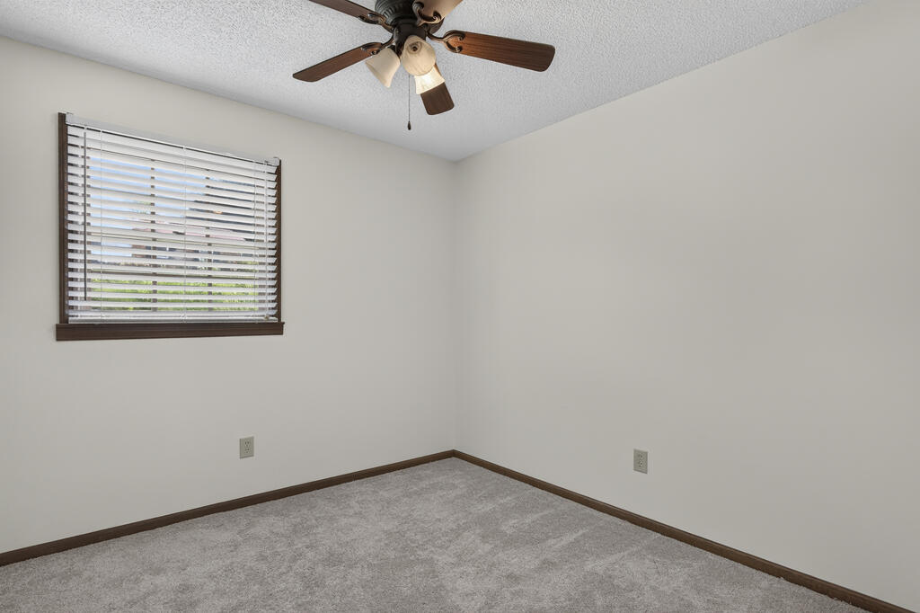 Empty bedroom with gray carpet, a ceiling fan, and a window with blinds.