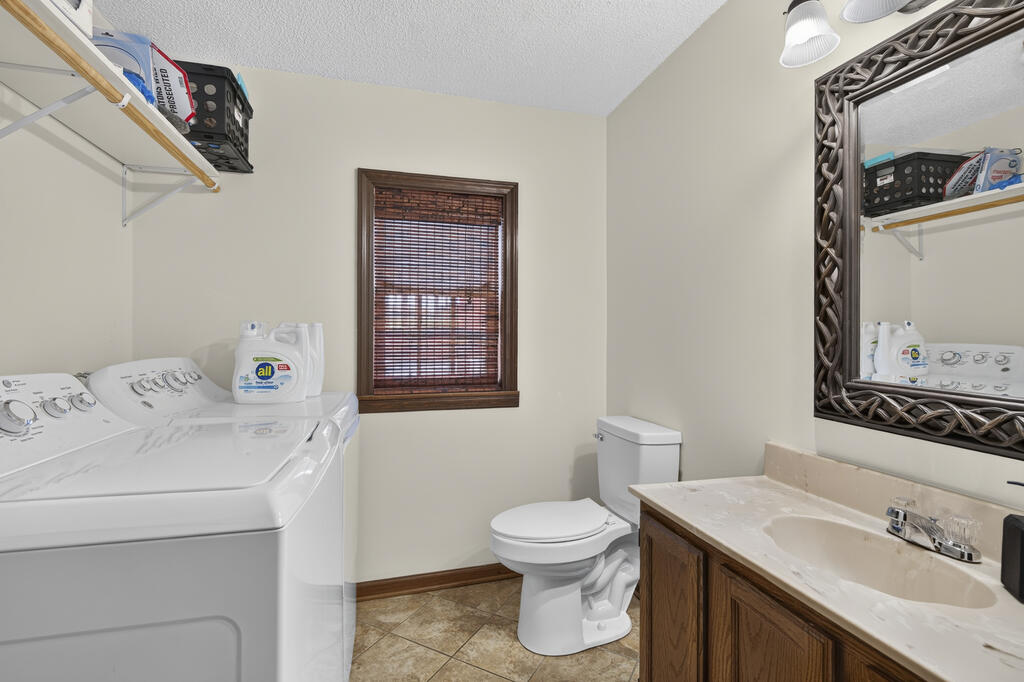 Laundry room with a washing machine, toilet, and wood vanity beneath a large framed mirror.