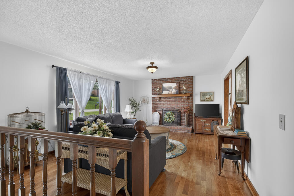 Living room with a brick fireplace, hardwood floors, and large curtained windows.