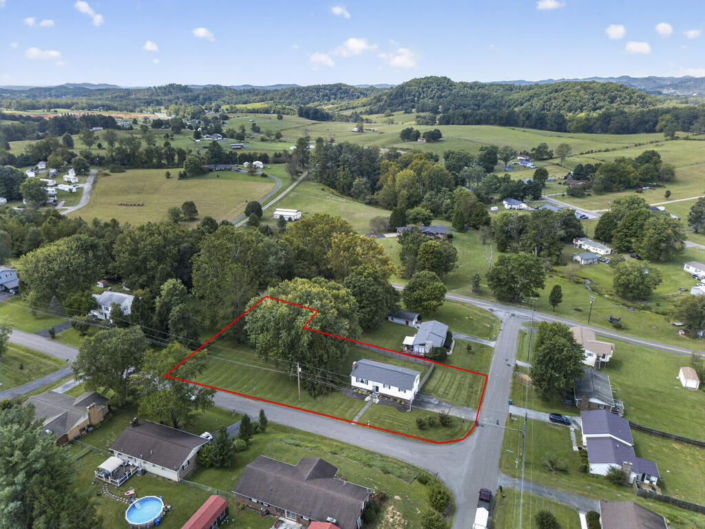Aerial view of a house and red-outlined lot amid rolling countryside and wooded hills.