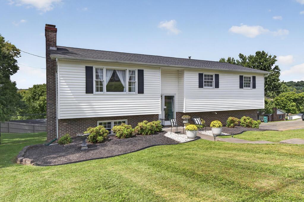 Split-level house with white siding, brick lower level, and a landscaped lawn with patio seating.