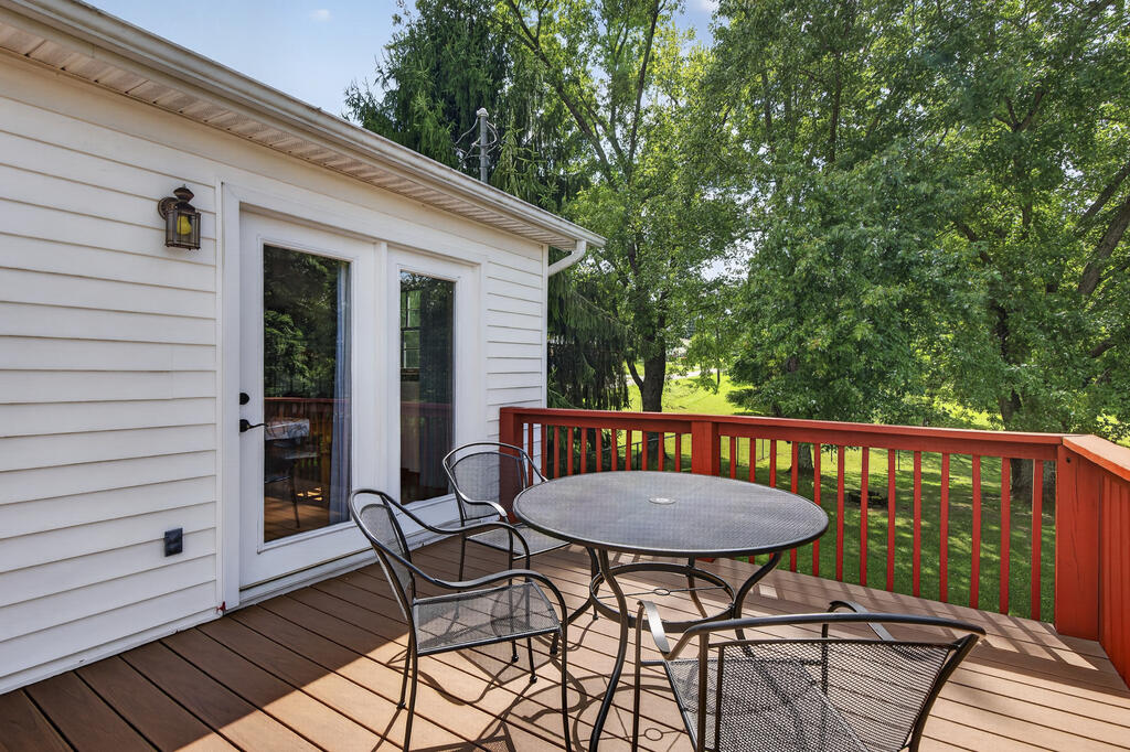 Brown deck with a round patio table and metal chairs overlooking a leafy yard.
