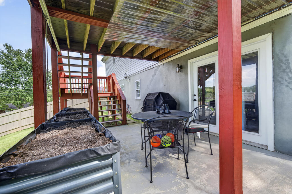 Covered patio with red deck supports, metal seating, and raised garden beds.