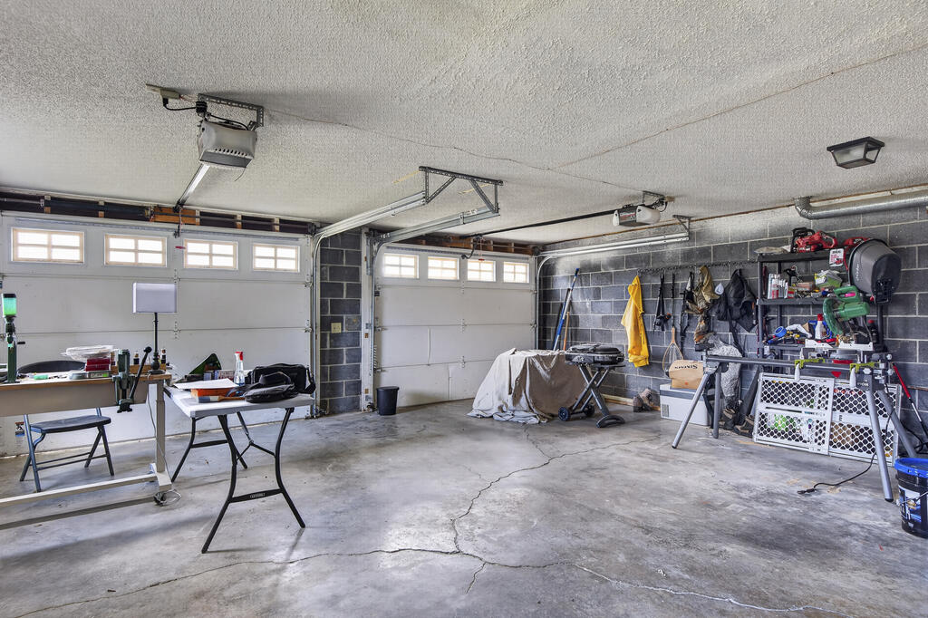 Two-car garage with overhead doors, worktables, and tools along the walls.