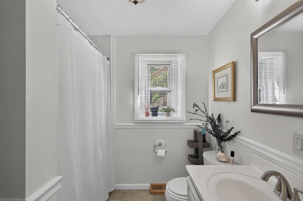 Bathroom with a white shower curtain, sink vanity, and a window with blinds.