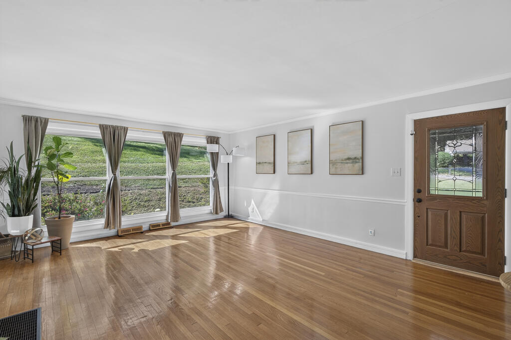 Empty living room with polished hardwood floors, curtained windows, and a wood door with decorative glass.