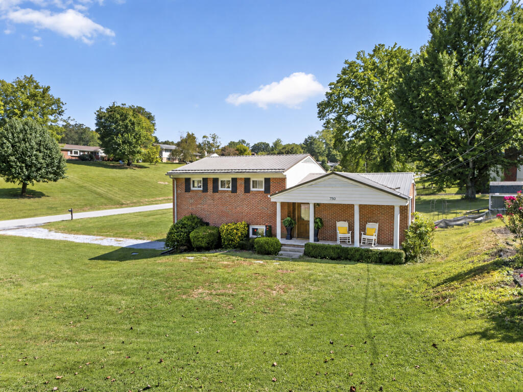 Two-story brick house with a covered porch and broad lawn on a sunny day.