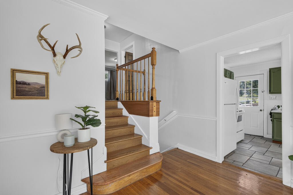 Foyer with a curved wood staircase, hardwood floors, and a view into the kitchen.