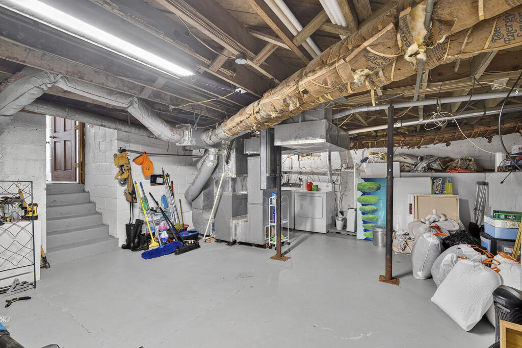 Basement laundry area with exposed ductwork, washer and dryer, concrete floor, and stairs.