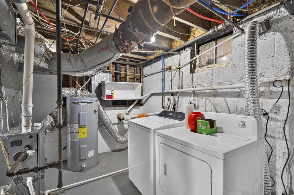 Basement laundry room with washer, dryer, water heater, and exposed pipes.